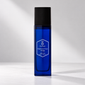 A Salveo Mathematics Toner Prestige skincare bottle in a deep cobalt blue glass with a matte black cap, standing on a light gray surface against a gray background with soft diagonal shadows.