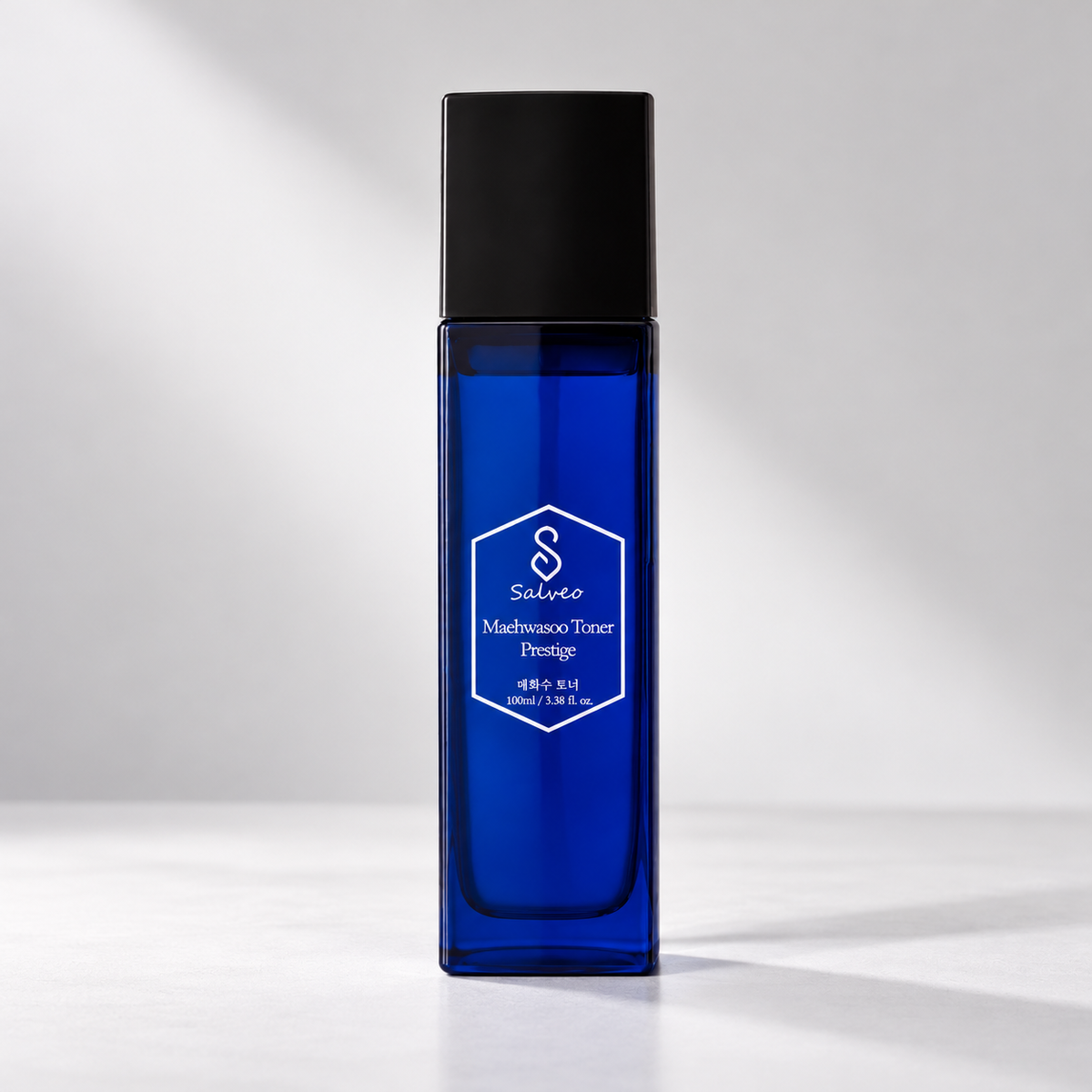 A Salveo Mathematics Toner Prestige skincare bottle in a deep cobalt blue glass with a matte black cap, standing on a light gray surface against a gray background with soft diagonal shadows.