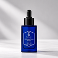 Salveo Madhwasoo Serum Prestige in a cobalt blue glass dropper bottle with a black cap, set against a light gray background with soft diagonal shadows.