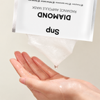 A hand receiving a clear, gel-like ampoule mask from a white foil packet labeled 'Diamond Radiance Ampoule Mask' by Snup, set against a soft beige background.