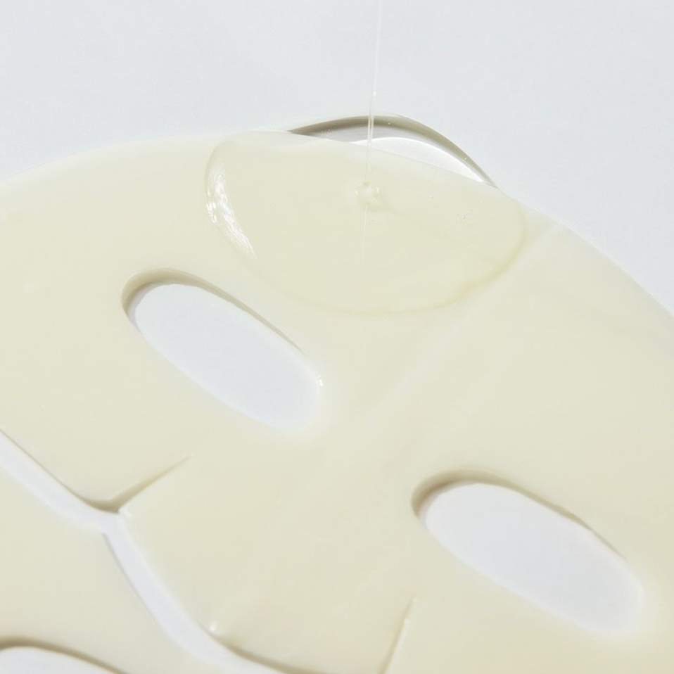 A close-up of a sheet mask with eye and mouth cutouts, shown inside a browser or app interface. The mask is a warm cream color, and the background is a light gray.